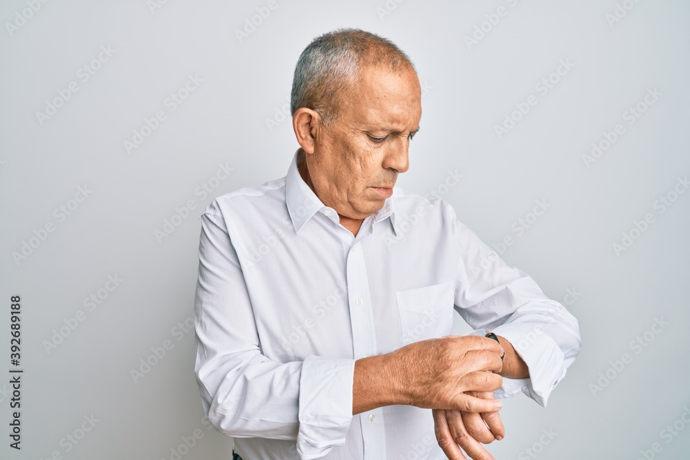 Handsome senior man wearing casual white shirt checking the time on wrist watch, relaxed and confident Handsome senior man wearing casual white shirt checking the time on wrist watch, relaxed and confident