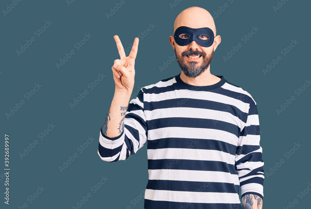 Naklejka premium Young handsome man wearing burglar mask showing and pointing up with fingers number two while smiling confident and happy.
