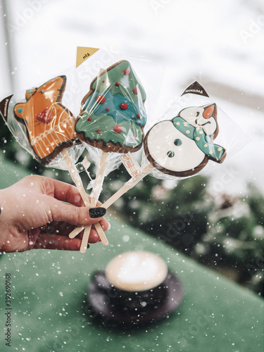 Christmas gingerbread in the hand. Sweets in the shape of a mouse, a Christmas tree and a snowman. In the background, a cup with coffee. Good New Year spirit. Drink coffee in the morning.