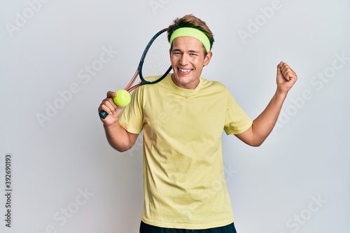 Handsome caucasian man playing tennis holding racket and ball screaming proud, celebrating victory and success very excited with raised arms © Krakenimages.com
