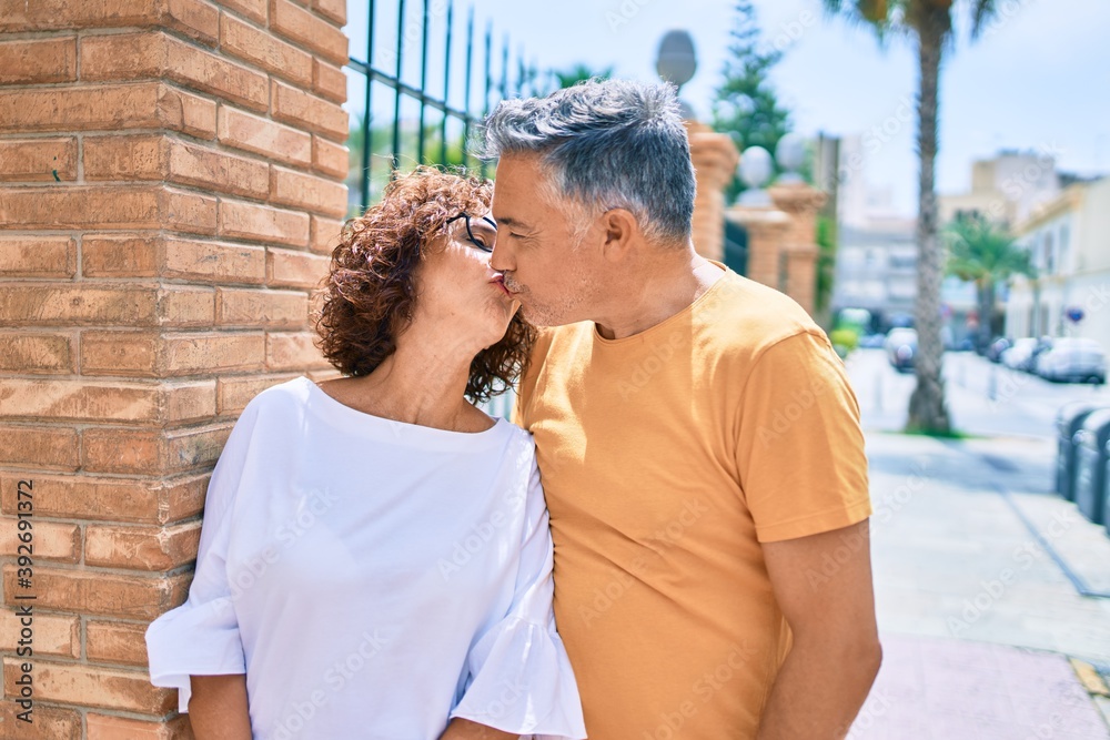 Middle age couple kissing leaning on the wall at street of city.