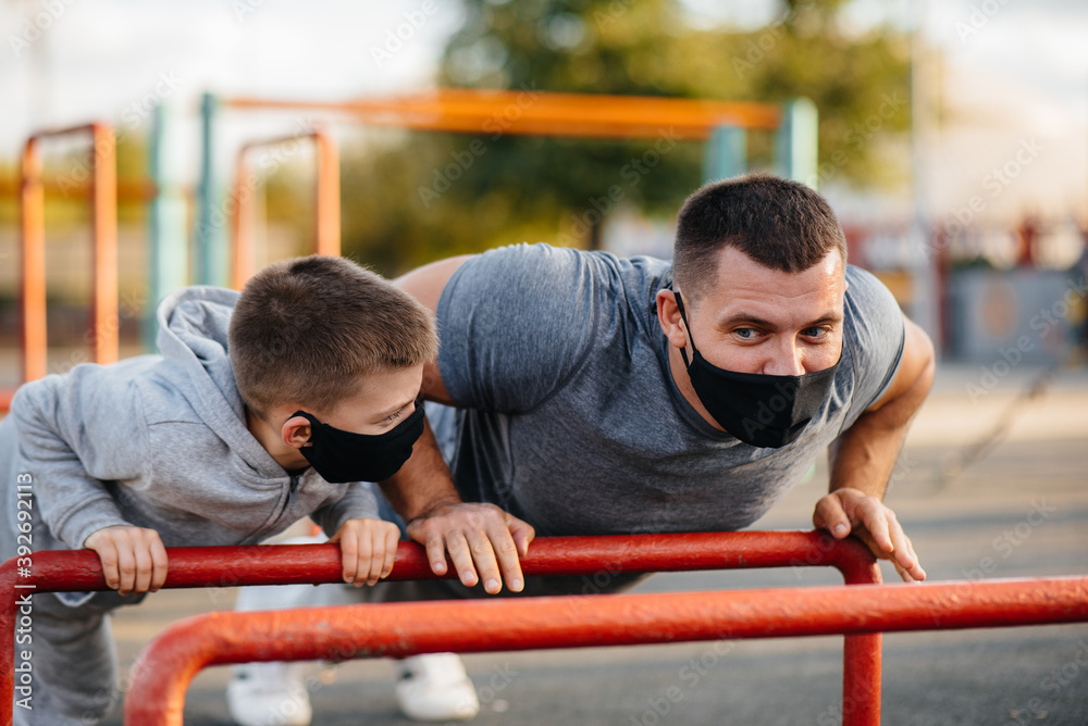 Obraz premium Father and son play sports on the sports field in masks during sunset. Healthy parenting and healthy lifestyle