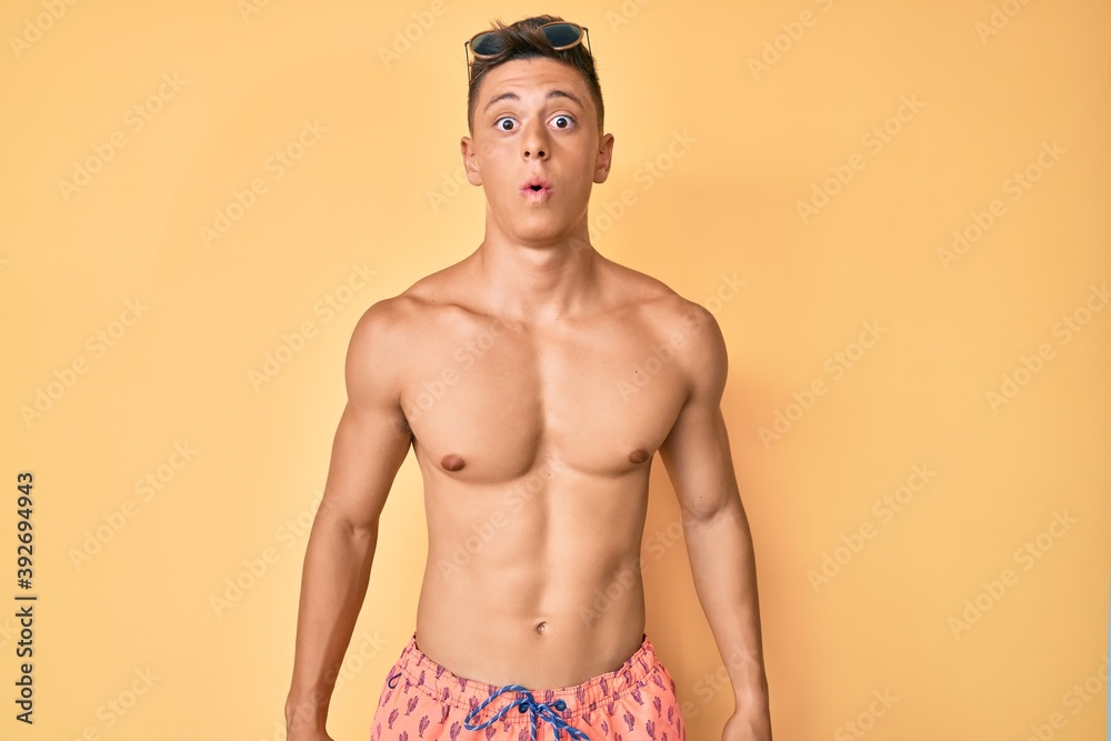 Young hispanic boy wearing swimwear shirtless scared and amazed with open mouth for surprise, disbelief face