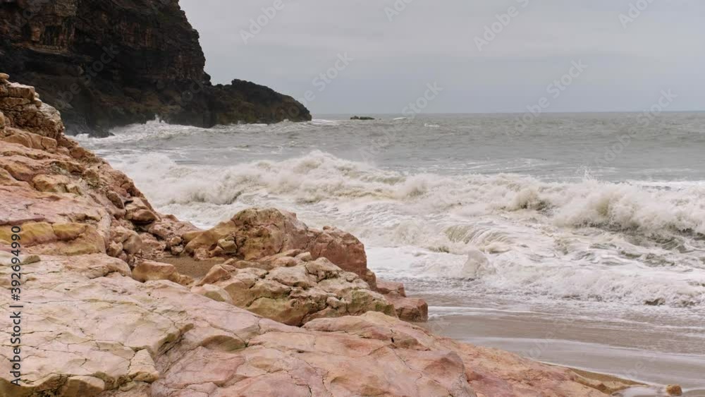 SLOW MOTION waves white with foam break on a sandy rocky cliff with dark stony mountains in the background, Cape Roca, Portugal SLOW MOTION waves white with foam break on a sandy rocky cliff with dark stony mountains in the background, Cape Roca, Portugal