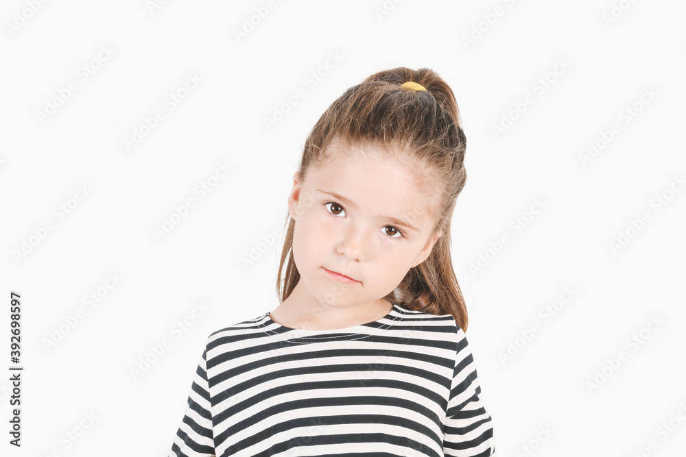Serious girl looking at camera with head tilted to one side. Posing little girl wearing striped shirt. Girl listening with attention. Serious girl looking at camera with head tilted to one side. Posing little girl wearing striped shirt. Girl listening with attention.