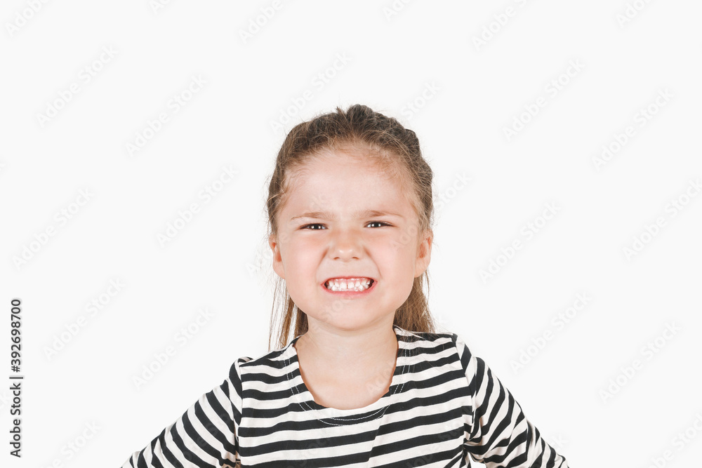 Angry girl looking at camera. Irritated girl with clenched teeth and open mouth is frowning face.. Posing a little girl wearing a striped shirt. Child can't handle her emotion. Dissatisfaction concept Angry girl looking at camera. Irritated girl with clenched teeth and open mouth is frowning face.. Posing a little girl wearing a striped shirt. Child can't handle her emotion. Dissatisfaction concept