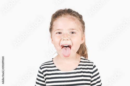 Funny girl showing tongue. Teasing, playing girl looking at camera with smiling eyes. Posing little girl wearing striped shirt.