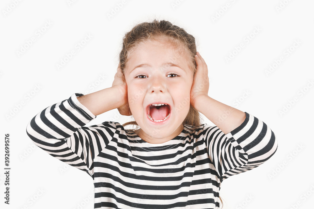 Loudly yelling girl with hands covering her ears. Girl is unwilling to listen, to hear something. Girl looking at camera. Posing little girl wearing striped shirt. Fear, rebellion concept. Loudly yelling girl with hands covering her ears. Girl is unwilling to listen, to hear something. Girl looking at camera. Posing little girl wearing striped shirt. Fear, rebellion concept.