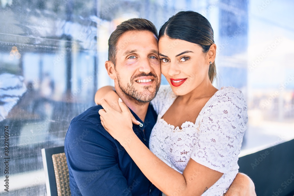 Fototapeta premium Young beautiful couple smiling happy and confident. Sitting with smile on face hugging at restaurant.