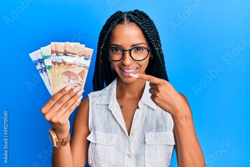 Beautiful hispanic woman holding canadian dollars smiling happy pointing with hand and finger photo