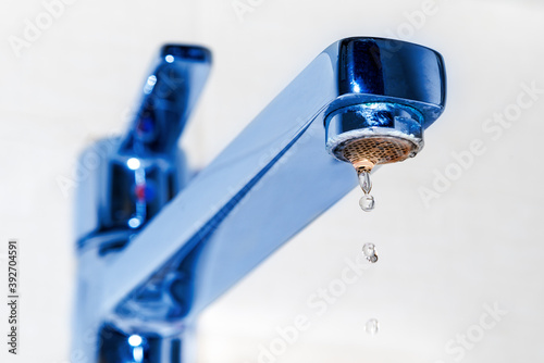 Water droplets drip from the chrome faucet in the kitchen sink or bathroom. The concept of the idea of saving water.
