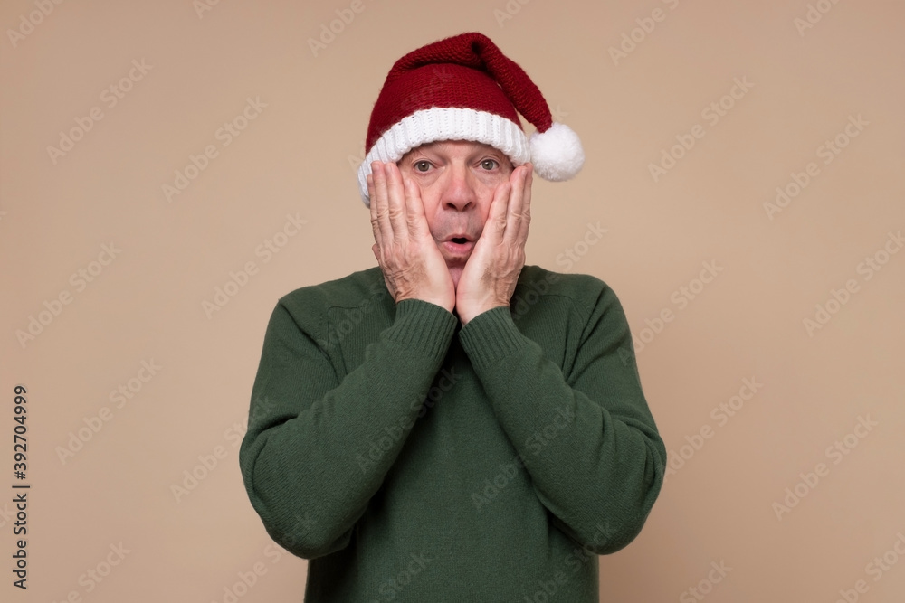 Surprised hispanic man wearing red christmas hat being shocked. Studio shot. New Year concept.