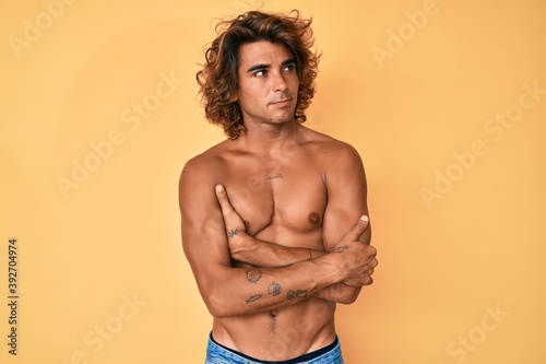 Young hispanic man standing shirtless looking to the side with arms crossed convinced and confident