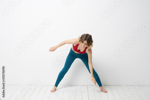 sports woman in a bright room doing yoga in full growth blue leggings and a red tank top