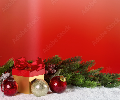 Christmas gift with balls, fir branch on the snow on a red background. New Year texture, postcard, idea.