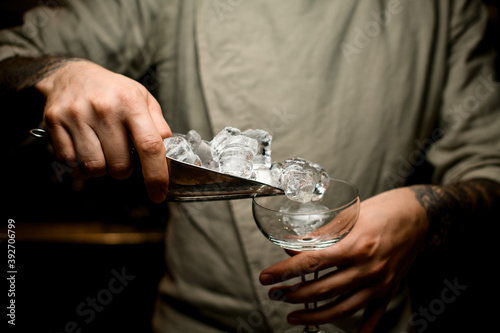 bartender holds metal scoop full of ice cubes and pours them into wine glass
