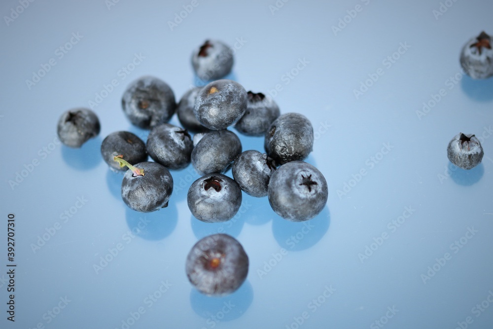 Fresh juicy Blueberries scattered and spilled over onto the surface of blue backlit background Fresh juicy Blueberries scattered and spilled over onto the surface of blue backlit background