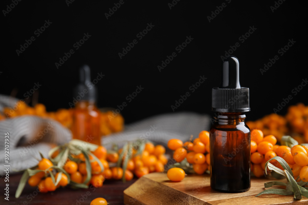 Ripe sea buckthorn and bottle of essential oil on wooden board against black background. Space for text Ripe sea buckthorn and bottle of essential oil on wooden board against black background. Space for text