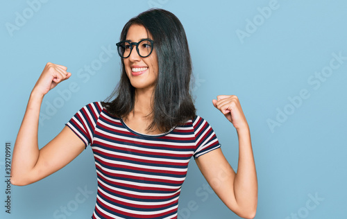 Beautiful asian young woman wearing casual clothes and glasses showing arms muscles smiling proud. fitness concept.