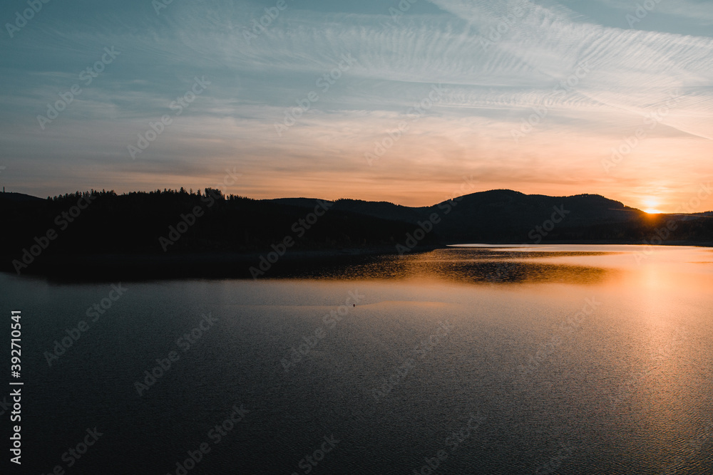 A beautiful sunset at a mountain lake with mountain silhouettes and warm orange light. Grane Dam, Granetalsperre, Harz Mountains