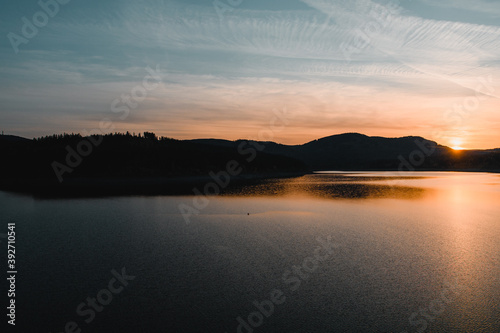 A beautiful sunset at a mountain lake with mountain silhouettes and warm orange light. Grane Dam, Granetalsperre, Harz Mountains