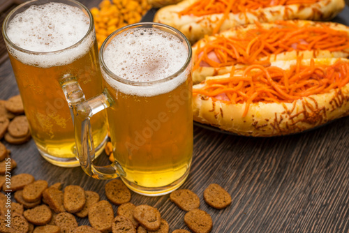 Two glasses of beer , hot dogs and snacks for beer on wooden table