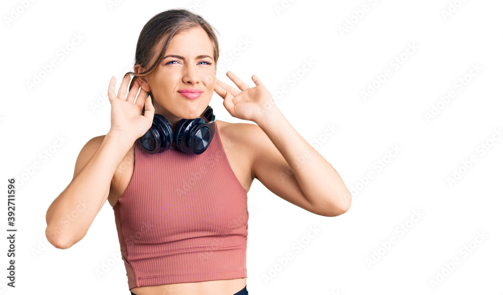 Beautiful caucasian young woman wearing gym clothes and using headphones trying to hear both hands on ear gesture, curious for gossip. hearing problem, deaf Beautiful caucasian young woman wearing gym clothes and using headphones trying to hear both hands on ear gesture, curious for gossip. hearing problem, deaf
