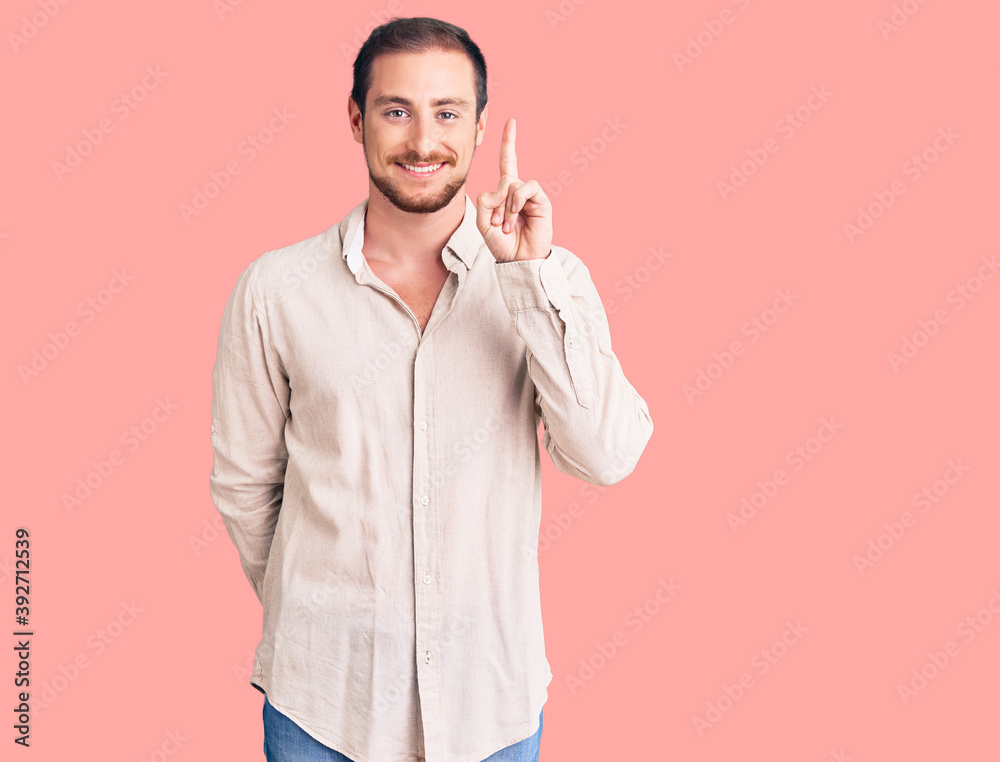 Young handsome caucasian man wearing casual clothes showing and pointing up with finger number one while smiling confident and happy. Young handsome caucasian man wearing casual clothes showing and pointing up with finger number one while smiling confident and happy.