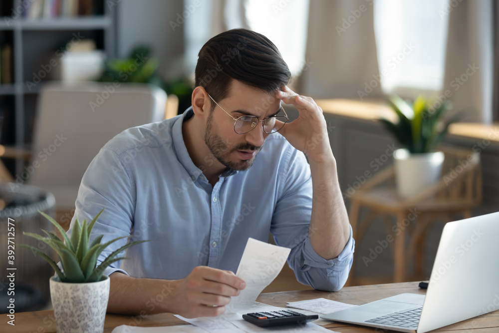 Small business owner experiences financial crisis, high costs, bank debt, money overspend concept. Man sitting at desk looks at laptop screen holding receipt feels desperate after calculating expenses Small business owner experiences financial crisis, high costs, bank debt, money overspend concept. Man sitting at desk looks at laptop screen holding receipt feels desperate after calculating expenses