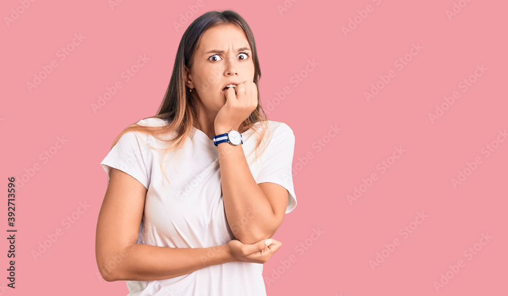 Beautiful caucasian woman wearing casual white tshirt looking stressed and nervous with hands on mouth biting nails. anxiety problem. Beautiful caucasian woman wearing casual white tshirt looking stressed and nervous with hands on mouth biting nails. anxiety problem.