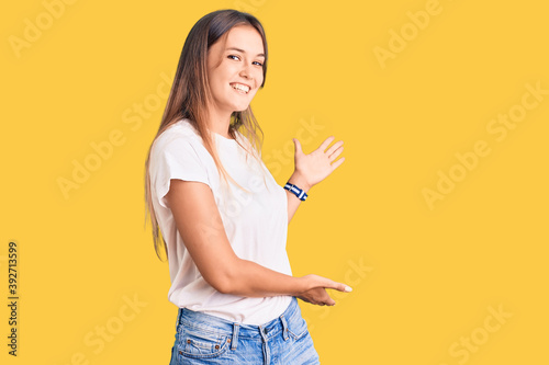 Beautiful caucasian woman wearing casual white tshirt inviting to enter smiling natural with open hand photo