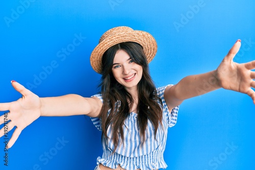 Young beautiful caucasian girl wearing summer hat looking at the camera smiling with open arms for hug. cheerful expression embracing happiness. © Krakenimages.com