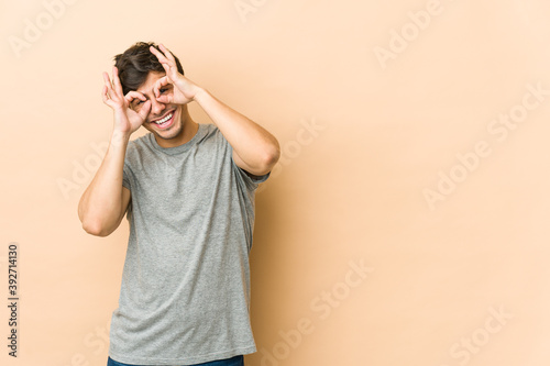 Young cool man showing okay sign over eyes