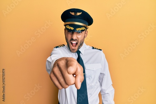 Handsome hispanic man wearing airplane pilot uniform pointing displeased and frustrated to the camera, angry and furious with you photo