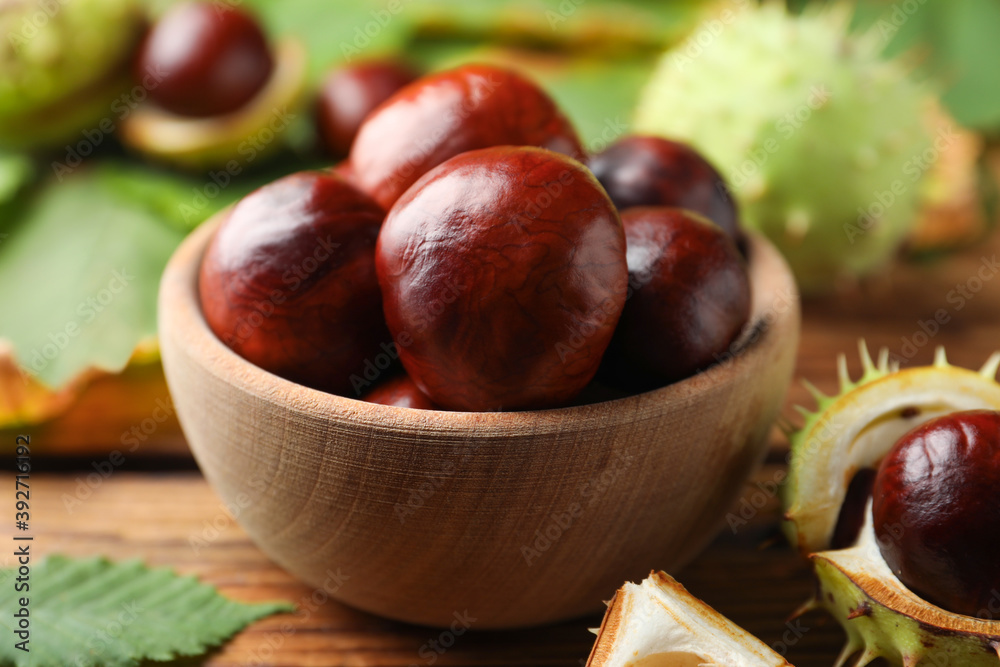 Horse chestnuts in bowl on wooden table, closeup Horse chestnuts in bowl on wooden table, closeup