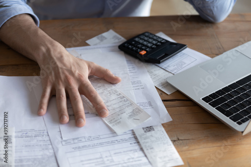 Individual entrepreneur make analysis of firm expenses, accountant do paperwork concept. On desk lot of receipts, calculator and laptop close up view. Man sit at table reviewing bills, managing budget