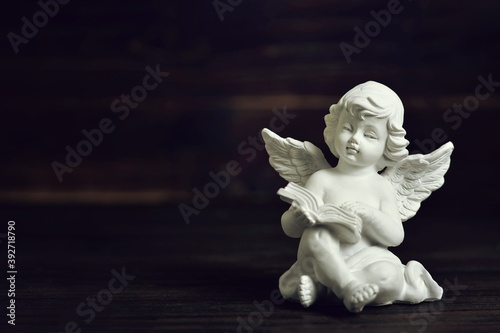 Fotografia Guardian angel sitting and holding a book on dark background with copy space
