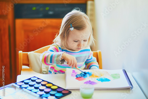 Adorable little girl drawing with colorful aquarelle paints