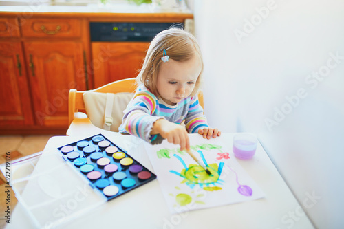 Adorable little girl drawing with colorful aquarelle paints