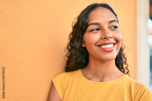 Young african american girl smiling happy leaning on the wall at city.