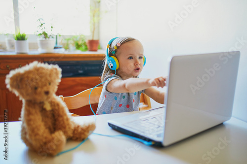 Toddler girl wearing eraphones with laptop photo