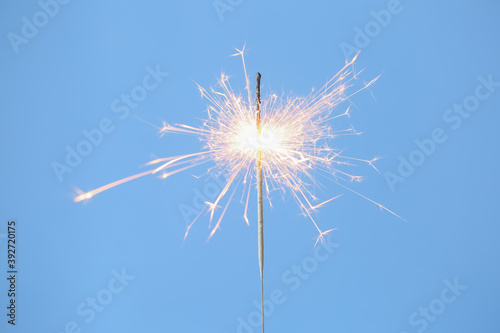 Bright burning sparkler on light blue background  closeup