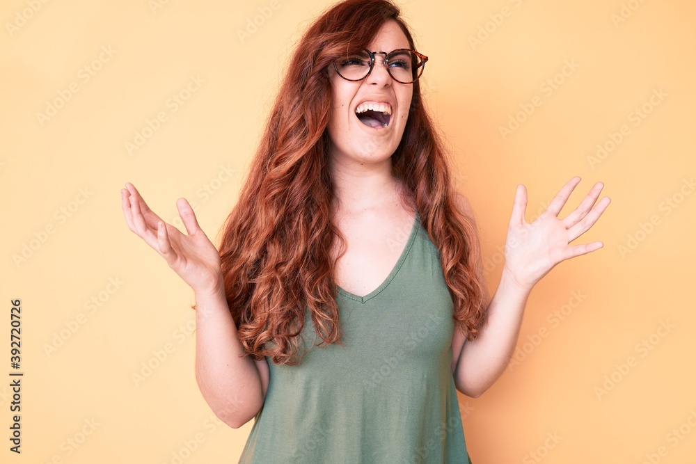 Young beautiful woman wearing casual clothes and glasses crazy and mad shouting and yelling with aggressive expression and arms raised. frustration concept. Young beautiful woman wearing casual clothes and glasses crazy and mad shouting and yelling with aggressive expression and arms raised. frustration concept.