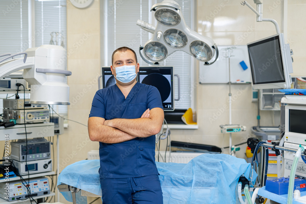Obraz premium Portrait of a male surgeon in mask standing arms crossed in operation room. Professional and confident doctor.