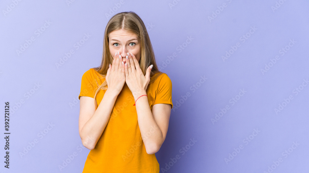 Young blonde woman isolated on purple background shocked, covering mouth with hands, anxious to discover something new.