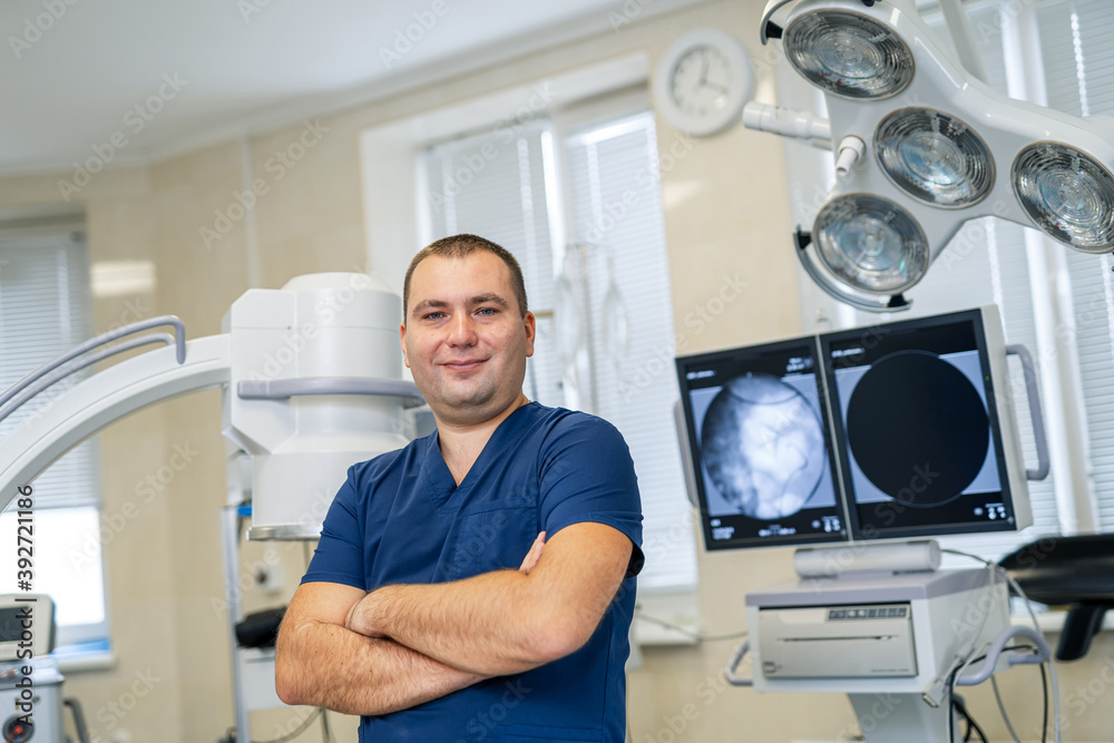 Portrait of an handsome doctor standing in hospital room. Medic smiles to the camera with crossed hands. Portrait of an handsome doctor standing in hospital room. Medic smiles to the camera with crossed hands.