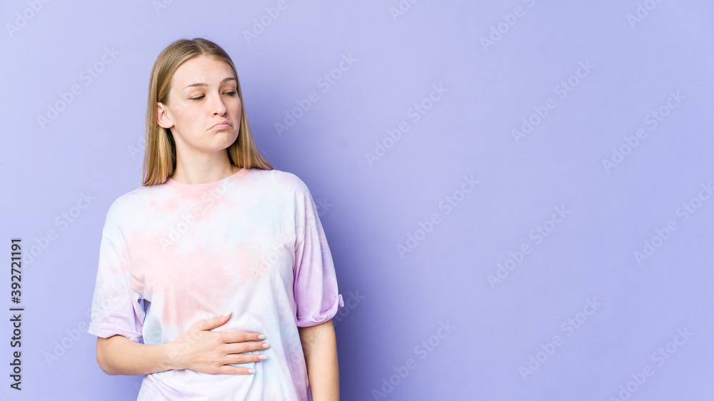 Young blonde woman isolated on purple background touches tummy, smiles gently, eating and satisfaction concept. Young blonde woman isolated on purple background touches tummy, smiles gently, eating and satisfaction concept.