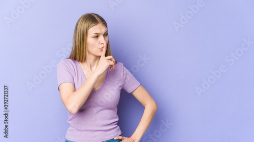 Young blonde woman isolated on purple background keeping a secret or asking for silence. © Asier