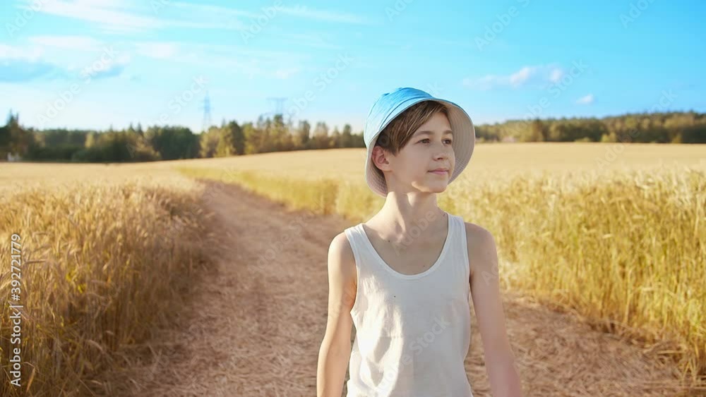 boy in a blue hat walking along the road in the wheat field, sunny weather boy in a blue hat walking along the road in the wheat field, sunny weather
