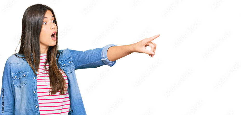 Young brunette woman wearing casual clothes pointing with finger surprised ahead, open mouth amazed expression, something on the front Young brunette woman wearing casual clothes pointing with finger surprised ahead, open mouth amazed expression, something on the front